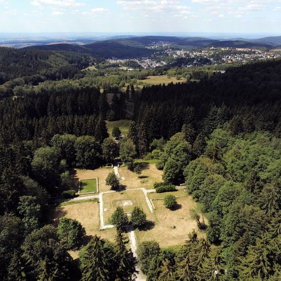 Drohnenaufnahme der Überreste des Kastell Kleiner Feldberg. Von oben ist nur wenig zu sehen. Das Kastell ist als größere Lichtung im Wald zu erkennen. Die ehemaligen Mauern sind als helle Linien auf dem Boden zu erkennen. 