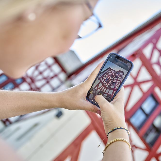 Ein Foto von einer Frau, die mit dem Handy ein Foto eines rot-weißen Fachwerkauses in Bad Camberg macht. 