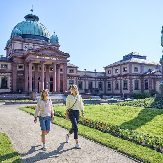 Zwei Frauen schlendern durch die Parkanlage vor dem Kaiser-Wilhelms-Bad in Bad Homburg. 