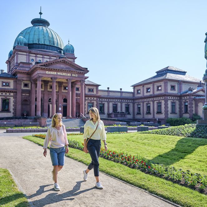 Zwei Frauen schlendern durch die Parkanlage vor dem Kaiser-Wilhelms-Bad in Bad Homburg. 