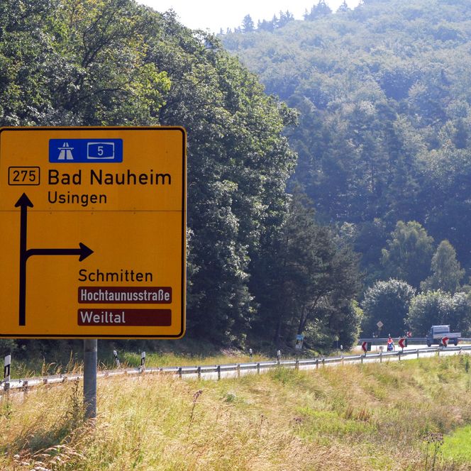 Auf einer Landstraße steht ein großes gelbes Verkehrsschild, das darauf hinweist, dass die Hochtaunusstraße nach rechts führt. 
