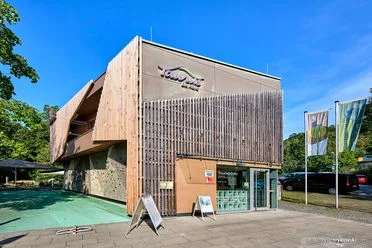 Außenaufnahme des Eingangs der Tourist-Information des Taunus-Informationszentrums. Die Fassade ist mit Holu verkleidet. An der Seite ist eine Boulderwand zu sehen. 