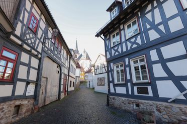 Gasse mit Fachwerkhäusern auf beiden Seiten. Am Ende der Gasse ist die imposante Kirche St. Ursula zu sehen. 