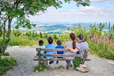 Eine Familie sitzt auf einer Bank und schaut in die hügelige Taunuslandschaft