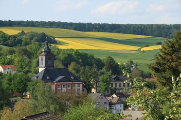 Die Evangelische Kirche in Grävenwiesbach mit einem kleinen aufgesetzten Türmchen liegt zentral im Ort. Der Ort ist eingebettet in Felder, die frühlingshaft blühen. 